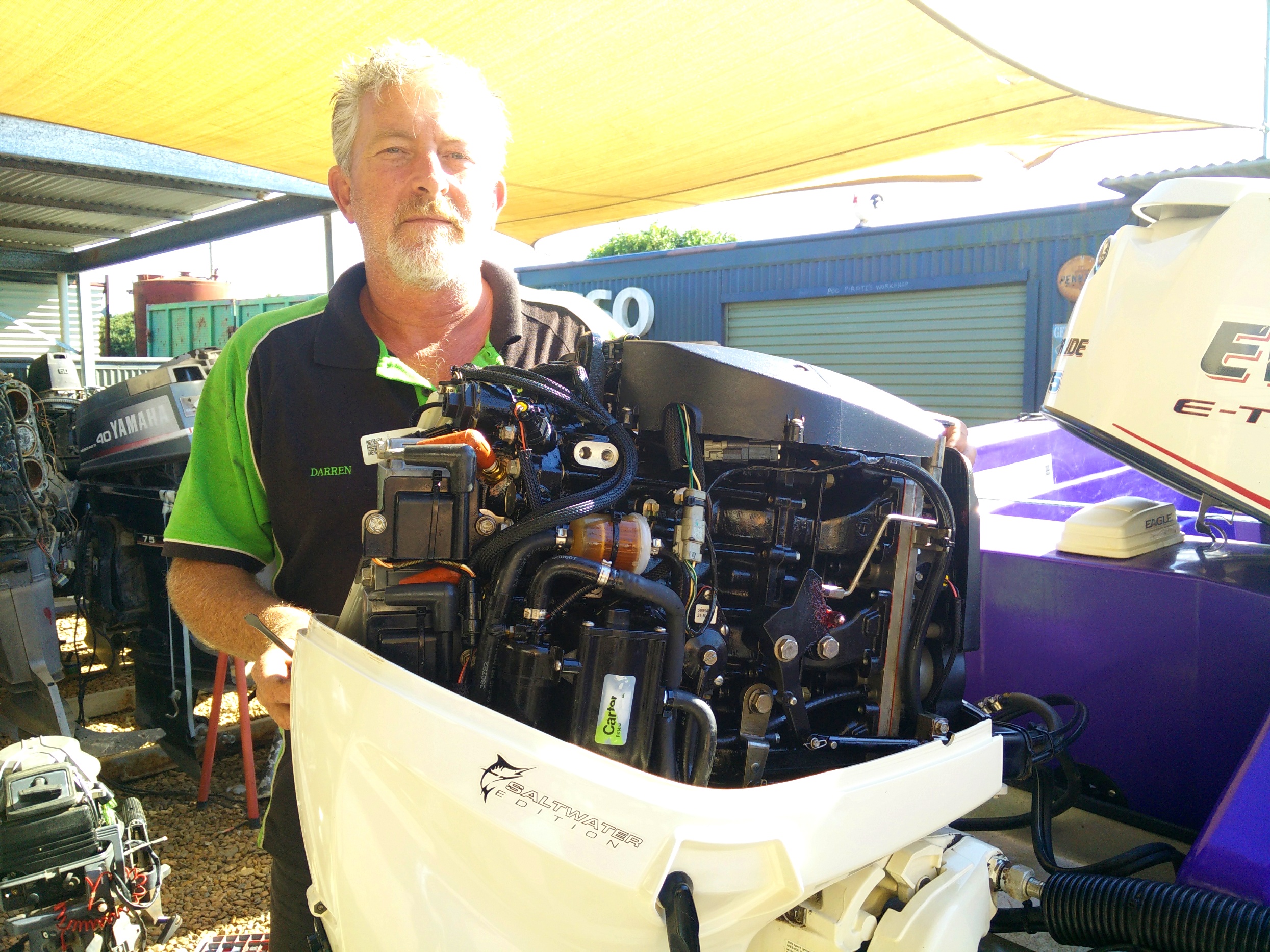 Darren Bowman holding a stripped outboard powerhead in the yard
