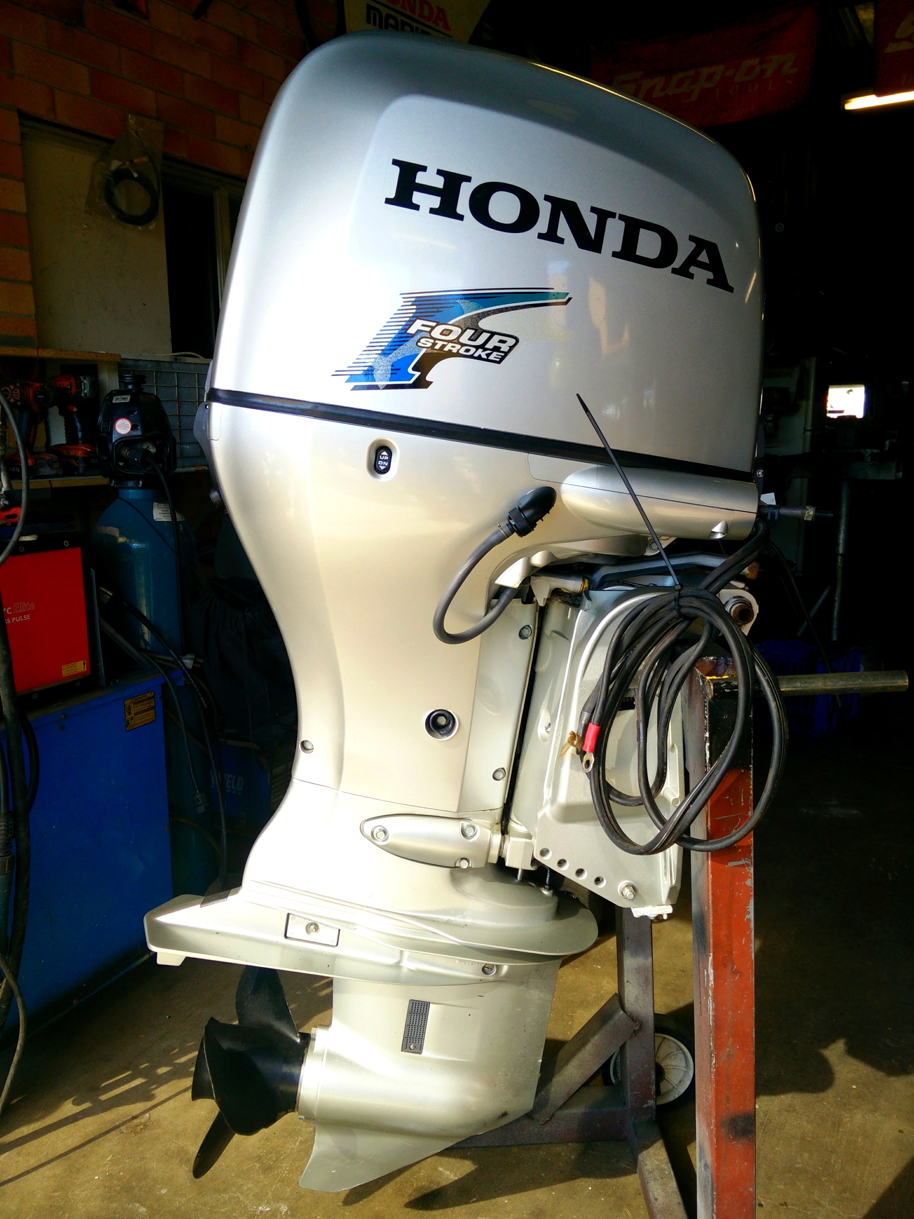 A Honda four stroke outboard on a stand inside the workshop